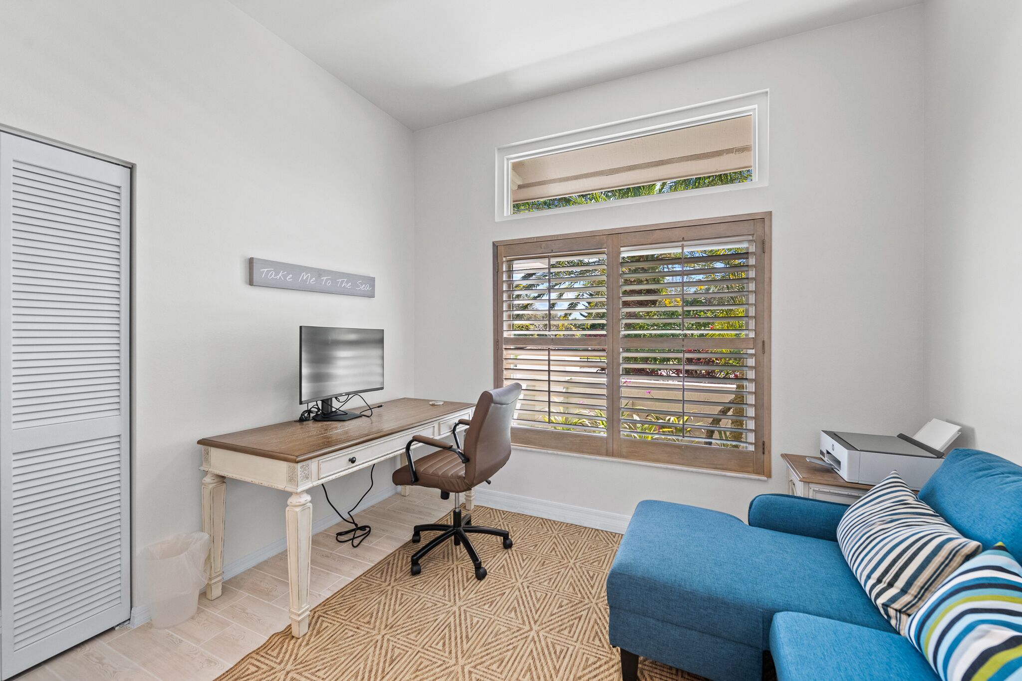 A room with a wooden desk, a computer, a blue sofa, and a window with blinds.