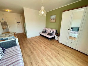 A bedroom with a bed, a wardrobe, a bedside table, a hanging light fixture, and a green wall. - Bright studio only 320mt from the sea (Porto Santa Margherita)
