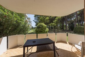 A patio area with a table and chairs, surrounded by a white fence, overlooking a garden with trees and a lawn. - Studio in a complex with 3 swimming pools (Bibione)