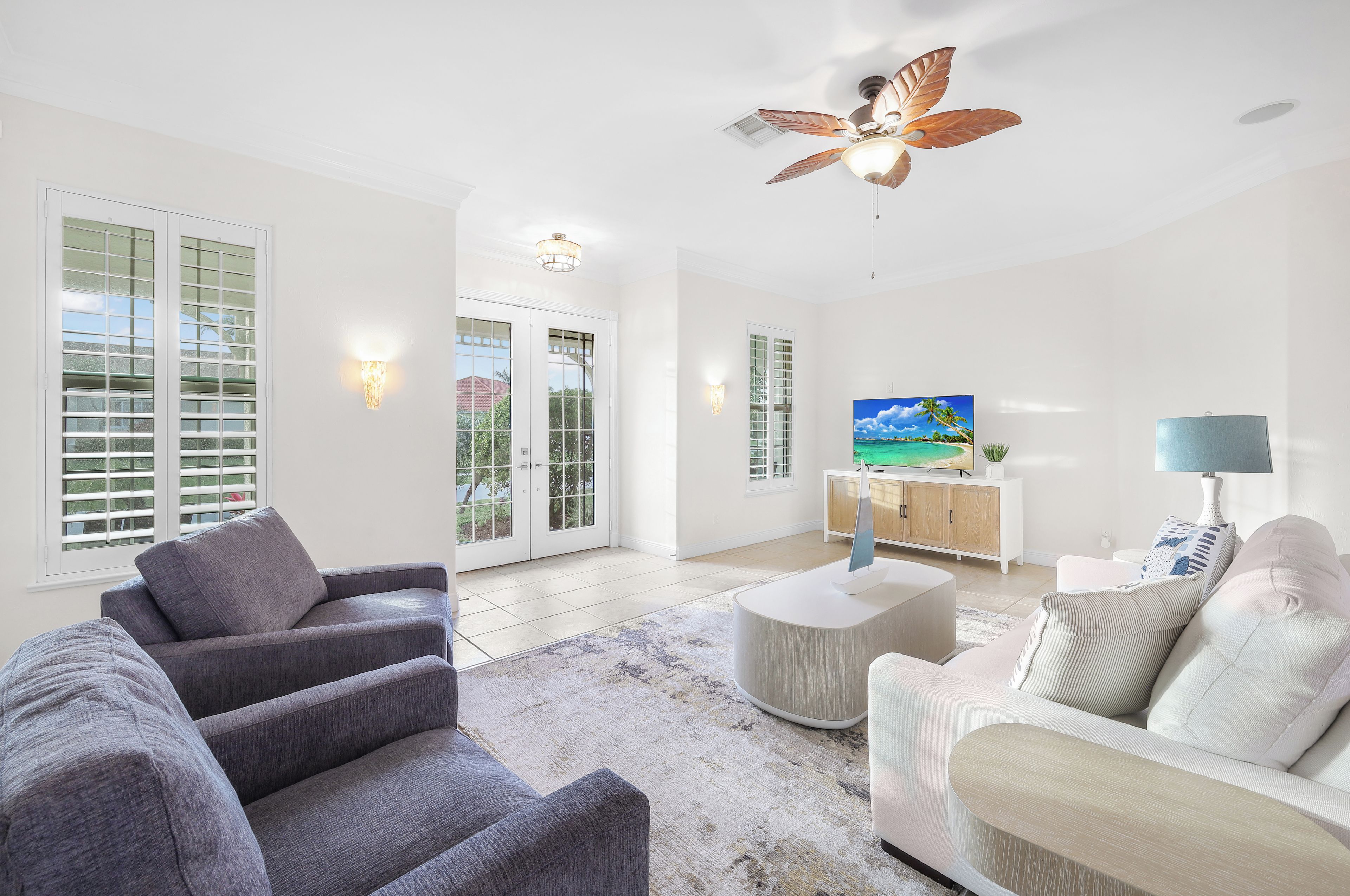 A spacious living room with a large TV, comfortable seating, and a ceiling fan.