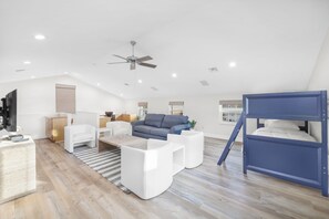 A modern loft bedroom with a sloped ceiling, a ceiling fan, a bunk bed, and a seating area with a sofa and chairs. - Coastal Two-Story Home | On Water w/ Pool/Dock (Marco Island)