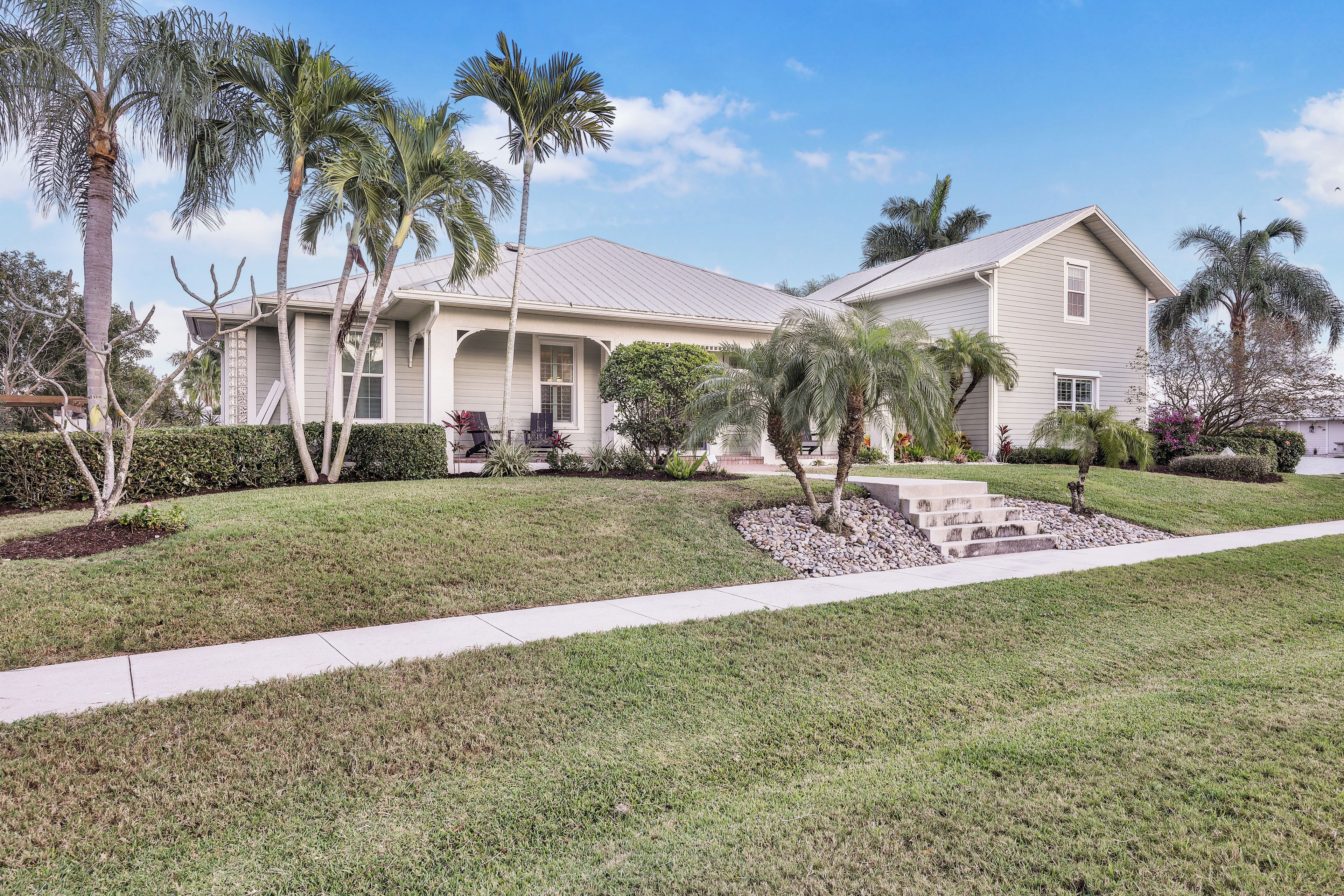 A two-story house with a covered porch, a well-maintained lawn, and palm trees.