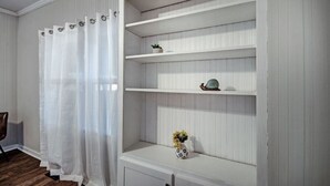 A room with a white wooden shelf unit against a wall with vertical paneling. There is a white curtain on the left side, and a small potted plant on the top shelf. - 50s Retro residence in picturesque neighborhood (Jackson)