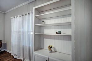 A room with a white wooden shelf unit against a wall with vertical paneling. There is a white curtain on the left side, and a small potted plant on the top shelf. - 50s Retro residence in picturesque neighborhood (Jackson)