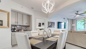Une cuisine moderne avec des meubles blancs, une table à manger entourée de chaises blanches et un ventilateur de plafond.