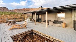 A wooden deck with lounge chairs, a table, and a fire pit. - Mountain Desert Retreat Elevation 40 Zion (Apple Valley)