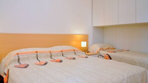 A hotel room with two beds, a nightstand, and a wall-mounted lamp. - Pinewood serenity just 100mt from the beach (Bibione)