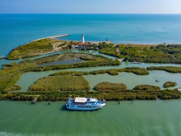 A riverboat docked at a marina surrounded by mangrove islands and a lighthouse in the distance.