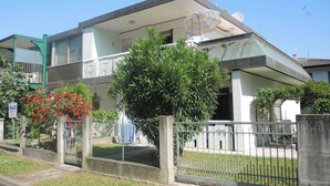 A two-story building with a flat roof and a large tree in front. - Bright apartment with garden (Bibione)
