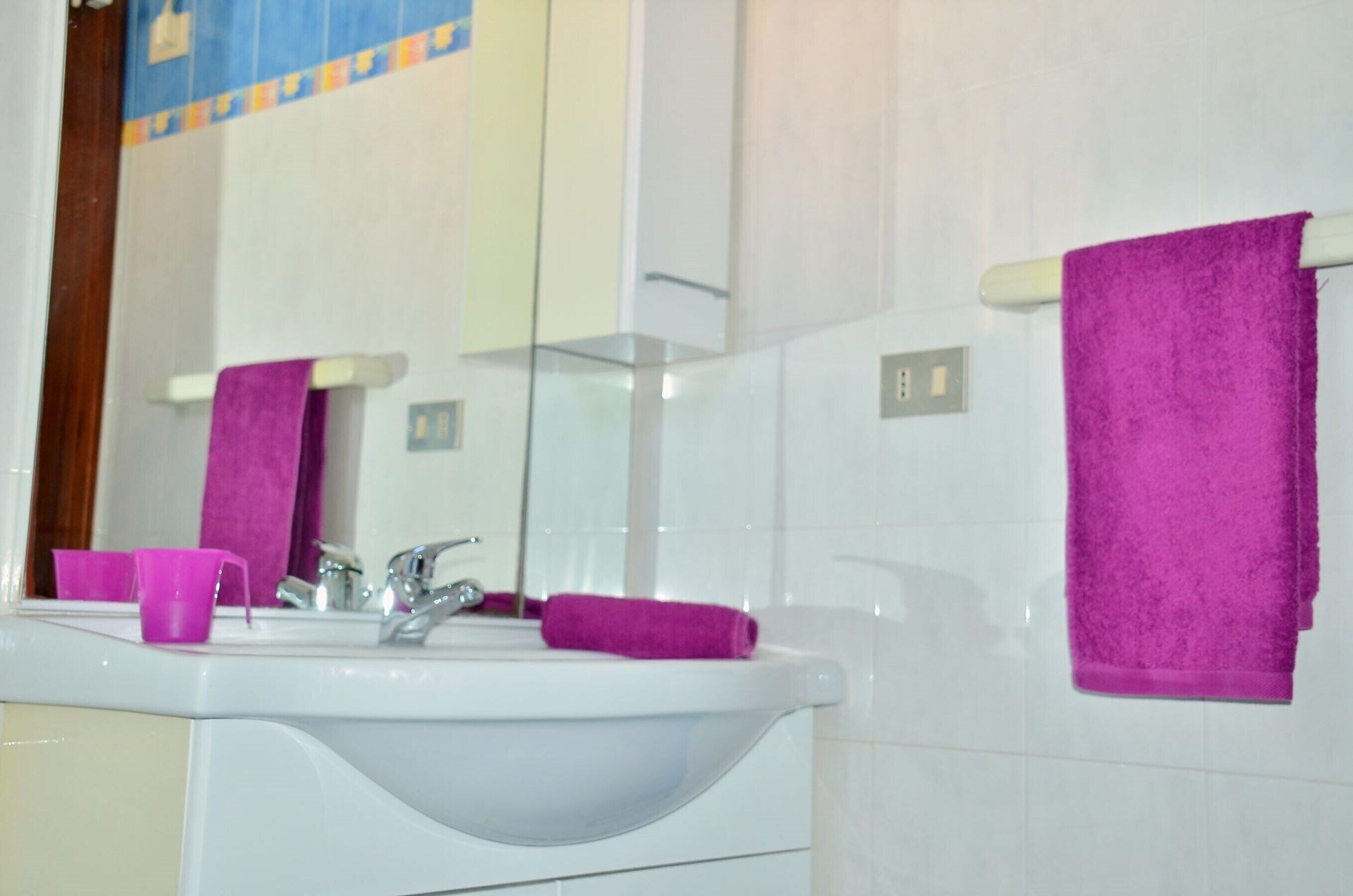 Un baño con un lavamanos blanco, un espejo y dos toallas moradas colgadas en la pared.