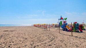 Een zandstrand met een speelplaats, inclusief kleurrijke glijbanen en speeltoestellen.