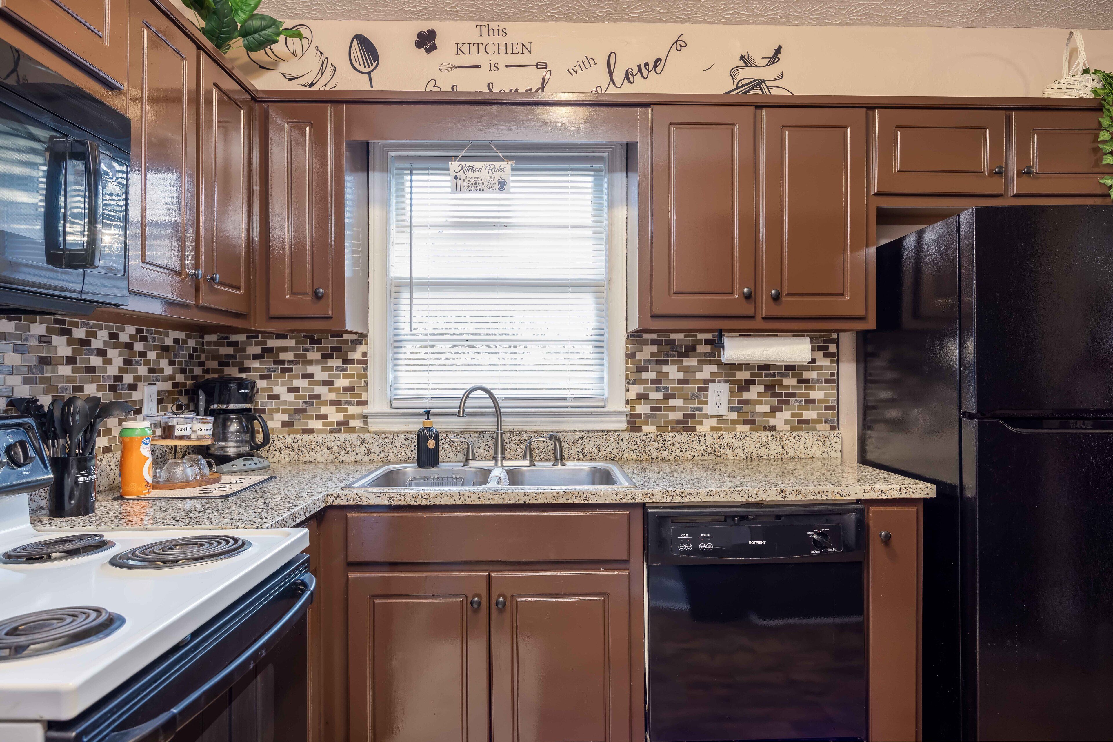 A kitchen with brown cabinets, a black refrigerator, a white stove, and a window with blinds.