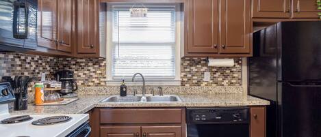 A kitchen with brown cabinets, a black refrigerator, a white stove, and a window with blinds.