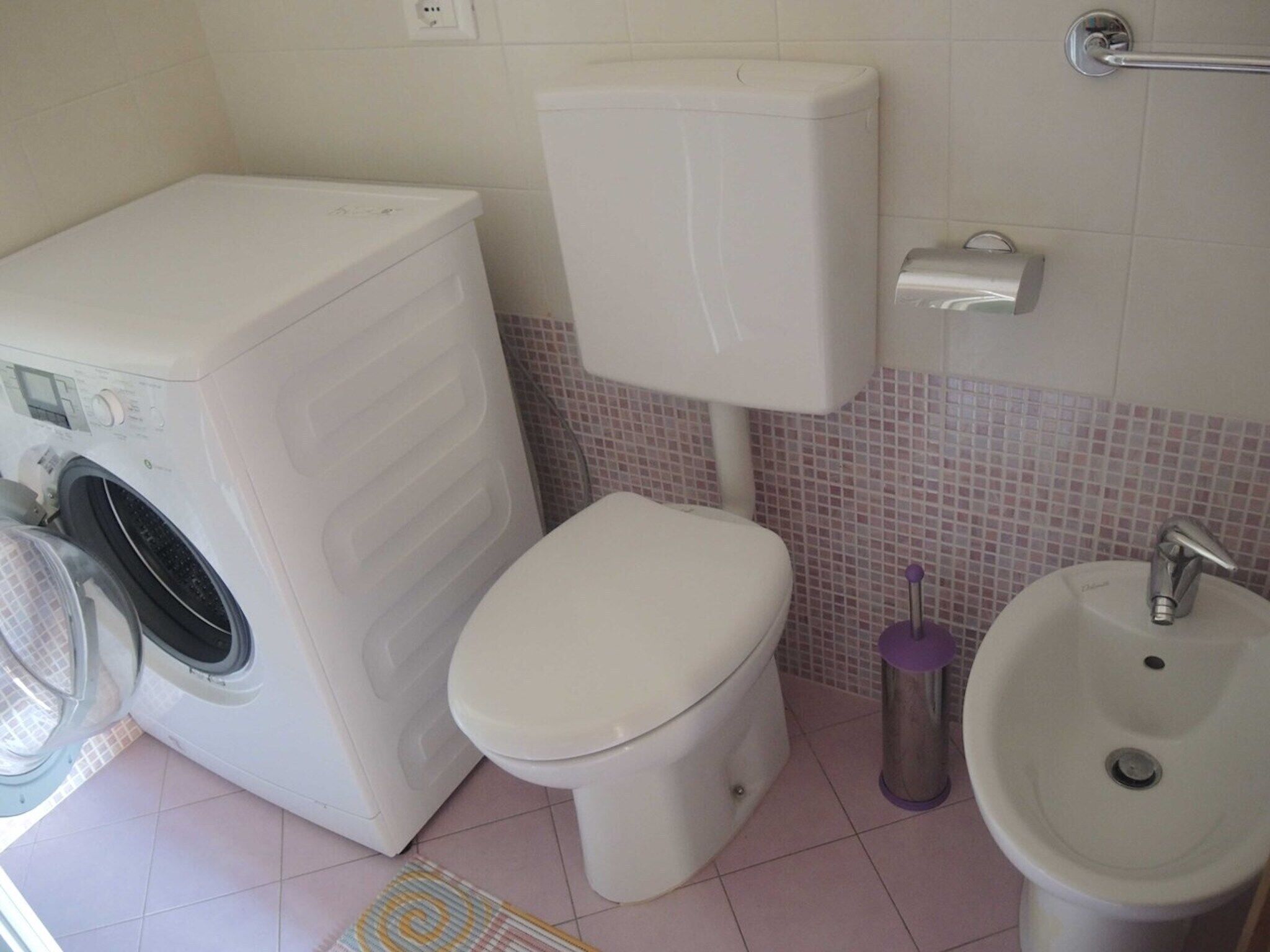 Casa de banho compacta com máquina de lavar, sanita e lavatório.
