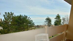 Un balcón con una mesa y sillas blancas, con vista a una zona residencial con árboles y casas.