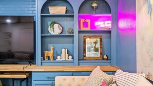 Una habitación con pared azul, un escritorio de madera, un sofá capitonado y estantes con objetos decorativos.