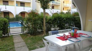 Un espace patio avec une table dressée pour les repas, une piscine et, au fond, un bâtiment doté de plusieurs balcons.