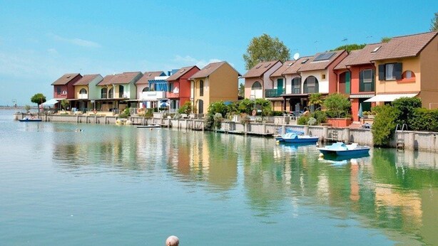 Une rangée de maisons colorées bordant un plan d’eau paisible où sont amarrés des bateaux.