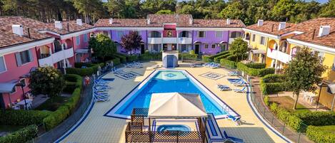A resort with a central swimming pool, sun loungers, and a covered area.