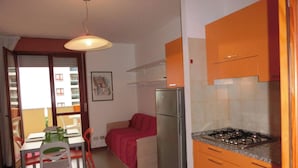 Eine kleine Küche mit orangefarbenen Schränken, einem Edelstahlkühlschrank und einem Gasherd.