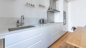 Una cocina moderna con armarios blancos, un lavamanos de acero inoxidable y una mesa de comedor de madera.