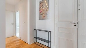 Un pasillo con suelo de madera, una puerta blanca, un estante de vidrio y una obra de arte enmarcada en la pared.