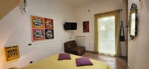 A bedroom with a bed, a chair, a TV, a window with curtains, and a wall-mounted mirror. - La Casetta con giardino al Pigneto (Rome)