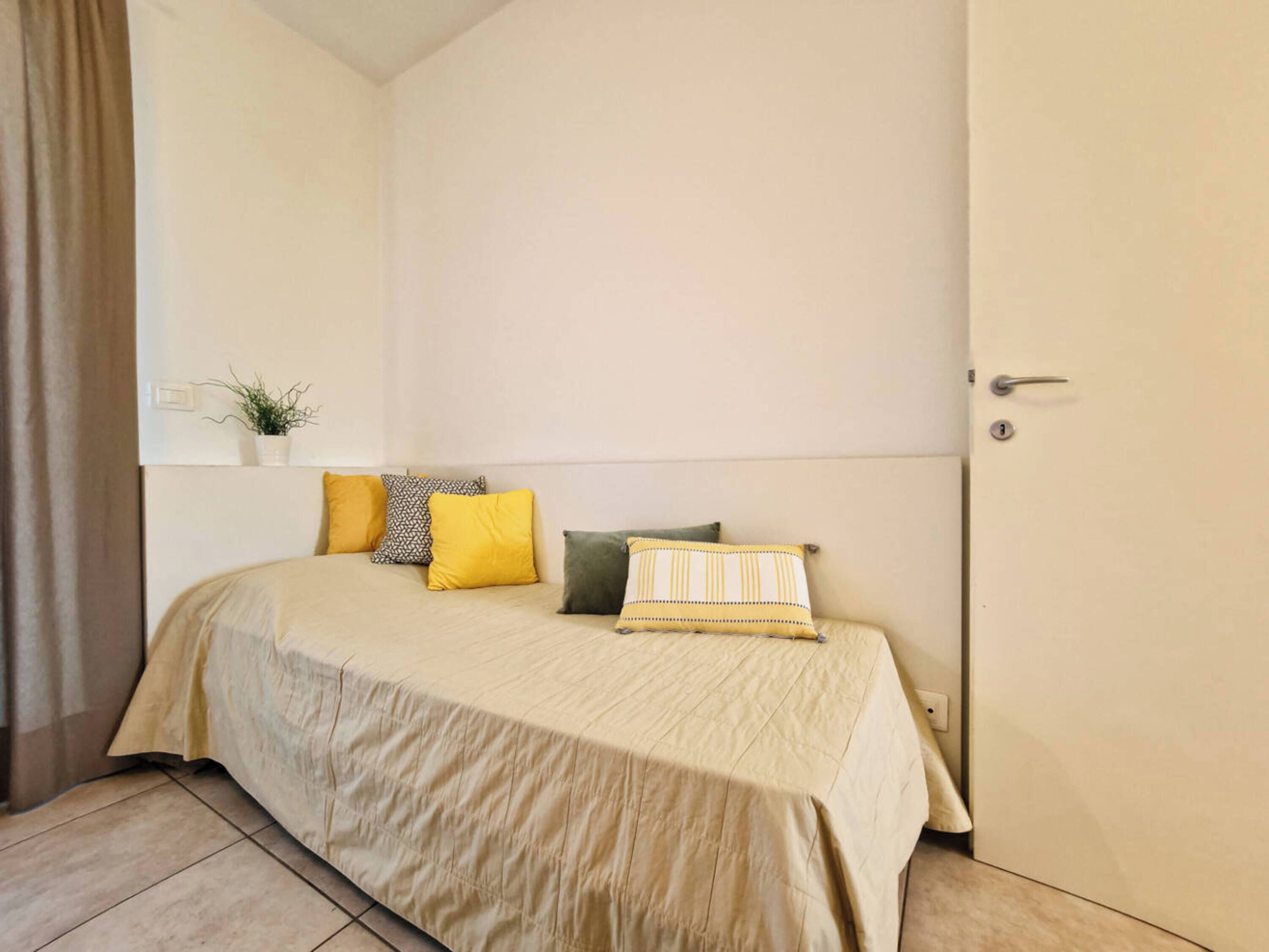 Ein Schlafzimmer mit einem Bett, Kissen, einer kleinen Pflanze und einer Tür.
