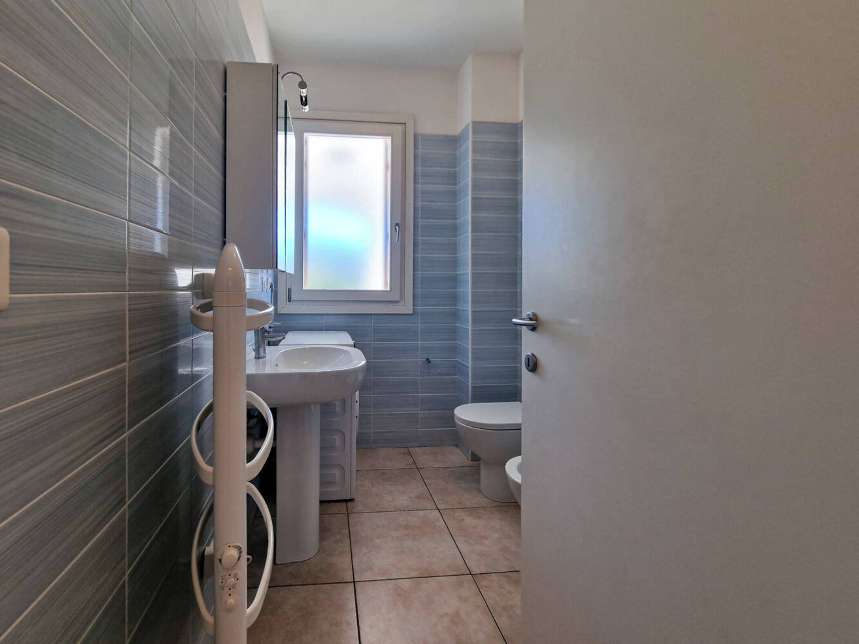 A modern bathroom with a large window, a sink, a toilet, and a washing machine.