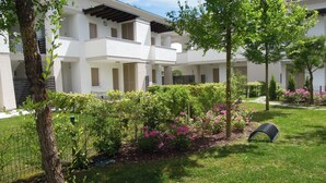 En moderne bygning med hvid facade, flere balkoner og en velplejet have med forskellige buske og blomster.