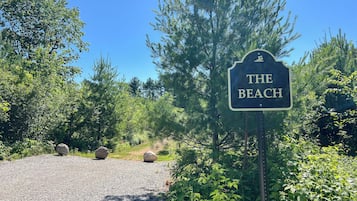 Opastekyltti, jossa lukee ”THE BEACH”, sijoitettu luonnonläheiseen ympäristöön, jossa on puita ja kivetty polku.