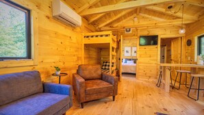 A cozy log cabin interior with a sofa, armchair, and a small table with a plant. - The Birch – New!  Menominee River Boutique Cottage (Porterfield)