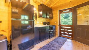 A compact kitchen with wooden walls, a refrigerator, cabinets, a microwave, and a stove. - The Birch – New!  Menominee River Boutique Cottage (Porterfield)