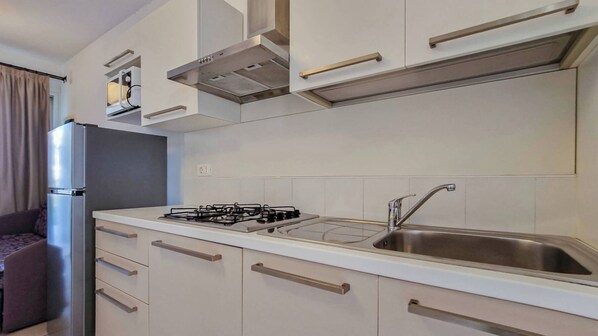 Una cocina moderna con armarios blancos, estufa a gas y pileta de acero inoxidable.