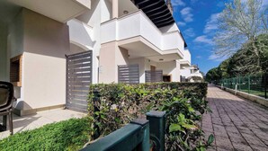 A modern residential building with a gated entrance, a paved pathway, and a green hedge.