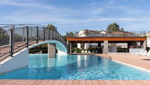 A swimming pool with a wooden deck, a curved metal railing, and a covered seating area with lounge chairs.