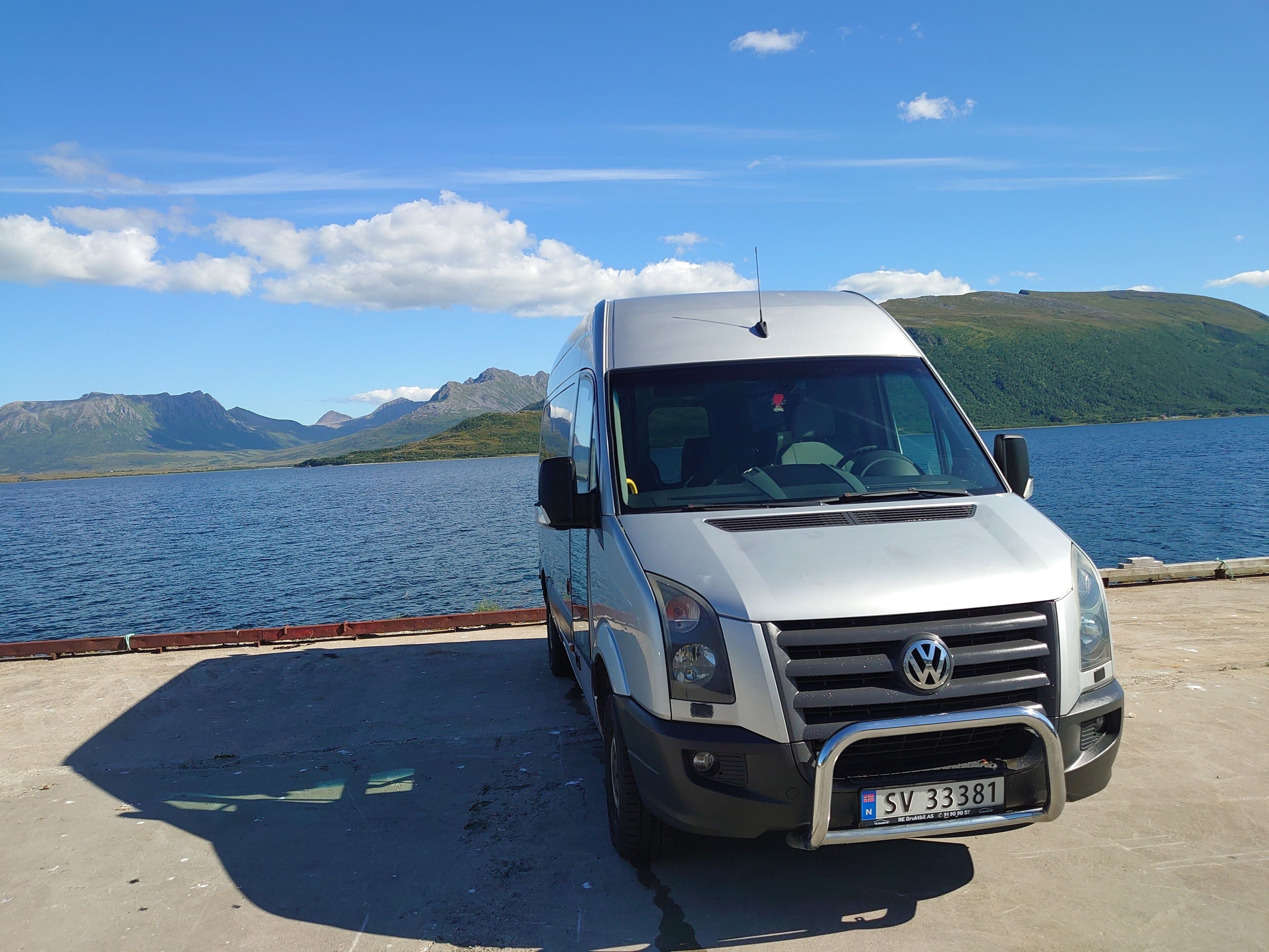 A white Volkswagen camper van parked by a lake with mountains in the background.