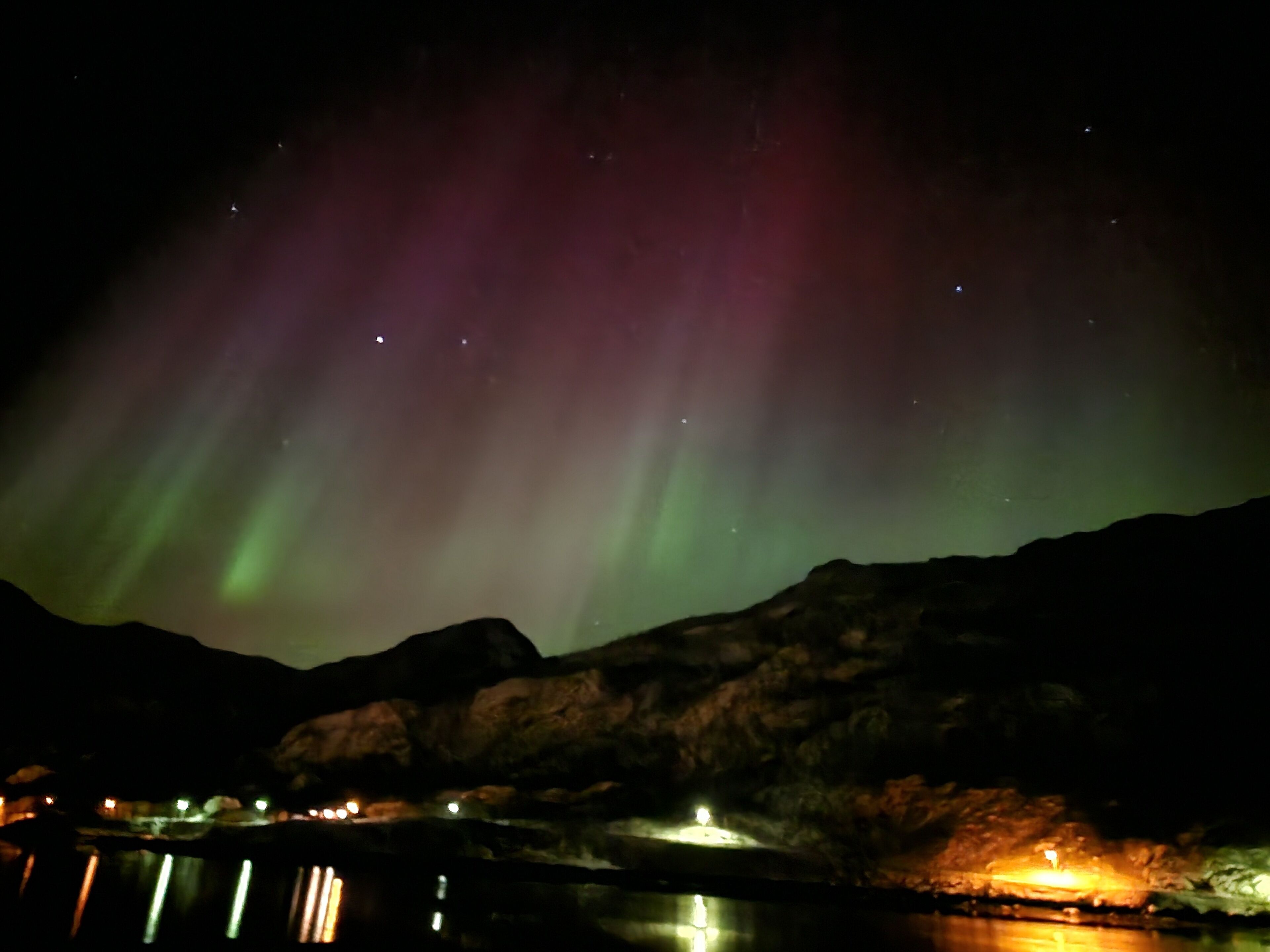 Una notte illuminata dall'aurora boreale su un paesaggio montuoso.