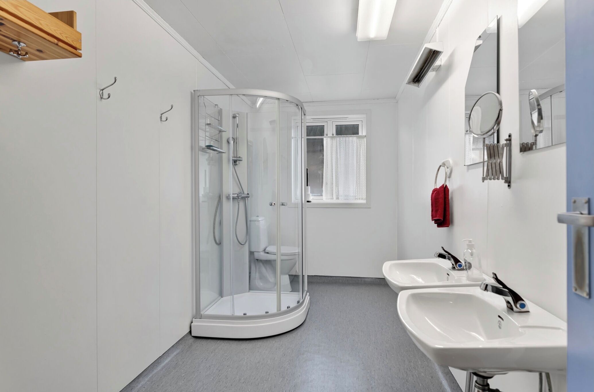 Un baño moderno con cabina de ducha de vidrio, dos lavamanos y un ventanal con cortinas.