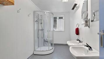 Un baño moderno con cabina de ducha de vidrio, dos lavamanos y un ventanal con cortinas.