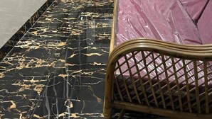 Una habitación con piso de mármol negro y dorado, dos sofás de mimbre con cojines morados y una pequeña mesa.
