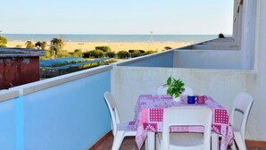 A balcony with a table and chairs, overlooking a beach with a clear sky. - Cozy studio flat with shared pool-Beahost (Bibione)