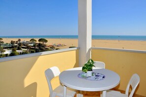 Un balcon avec vue sur la plage, une table ronde avec des chaises et une plante en pot.