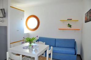 Une pièce avec une table blanche, un canapé bleu, un miroir rond et deux étagères remplies d’objets.