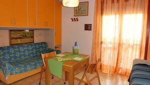 Une petite pièce agréable et chaleureuse, avec un canapé, une table à manger entourée de chaises, un luminaire suspendu et une fenêtre avec des rideaux.