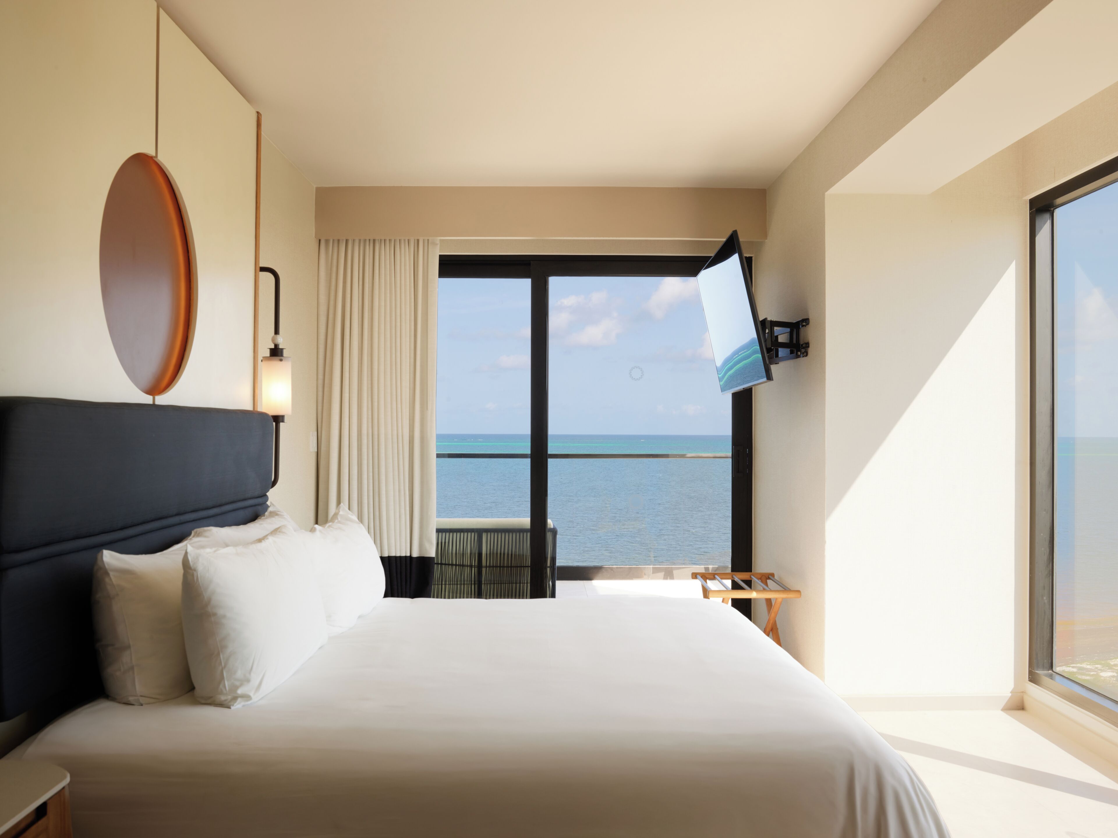 Habitació d'hotel amb un llit gran, televisió penjada a la paret, vista a l'oceà i un balcó amb taula i cadires.