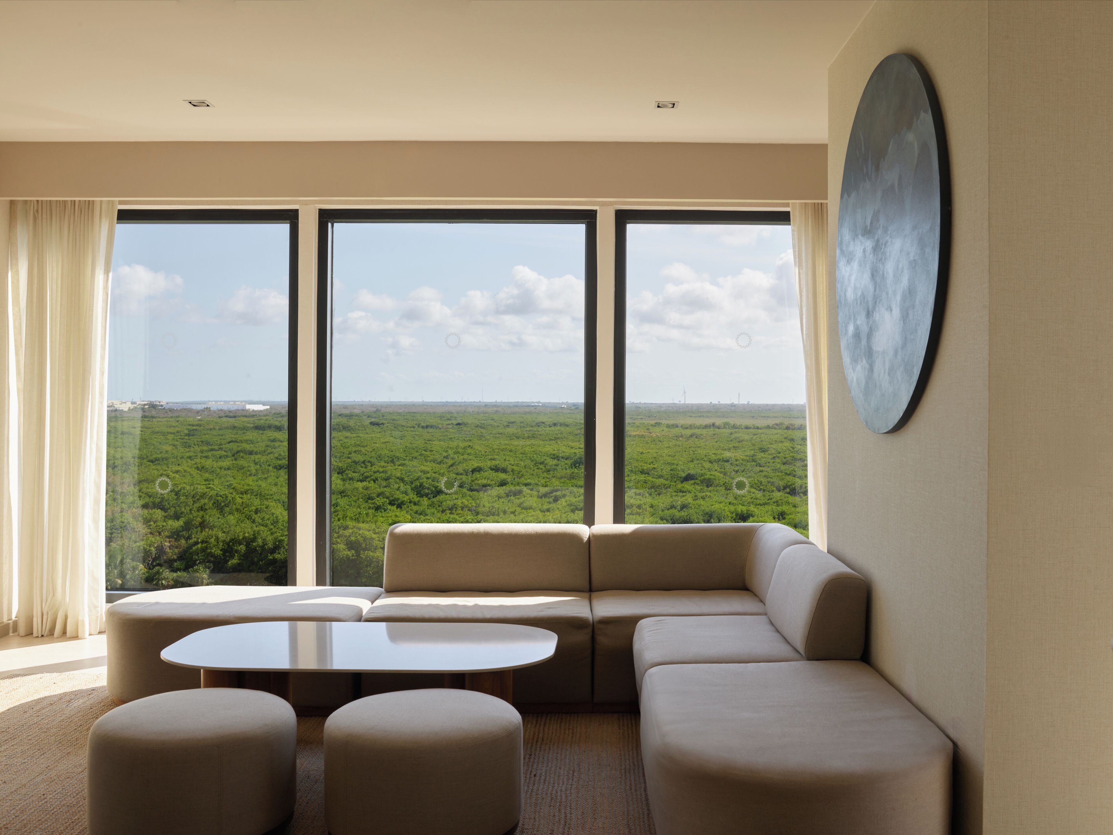 A modern living room with a large window, a sofa, ottomans, and a round table.