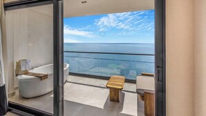A balcony with a view of the sea, a bathtub, and two wooden stools. - AVA Resort Cancun (Cancun)