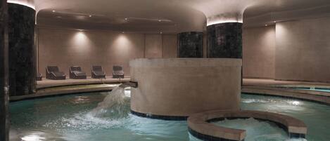 A spa area with a hot tub, lounge chairs, and a water feature.