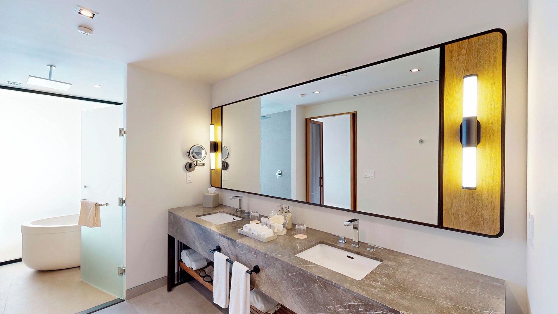 A modern bathroom with a large mirror, two sinks, and a glass shower enclosure.
